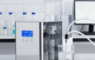 Laboratuvar ortamında çalışan dijital ekranlı saf su üretim cihazı ve cam behere doldurulan saf suyun detaylı yakın çekim görüntüsü.
